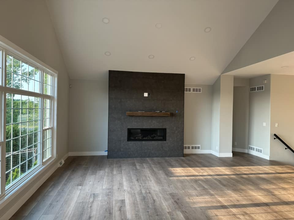 Finished great room with completed dark tile fireplace wall, raw wood mantel, linear fireplace, and large multi-pane windows